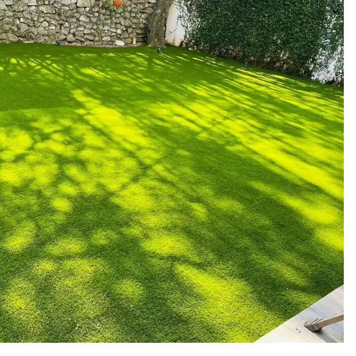 Jardín residencial con pasto sintético EasyGarden — sombras naturales de árboles sobre fibra verde
